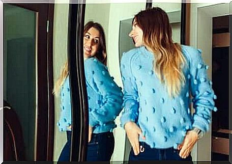 A woman wearing a sweater looking in the mirror.